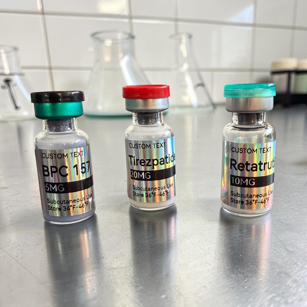Three small glass vials with holographic labels. The left vial has a dark green cap and reads BPC 157 5MG. The middle vial has a red cap and reads Tirezpatide 20MG. The right vial has a teal cap and reads Retatrutide 10MG.