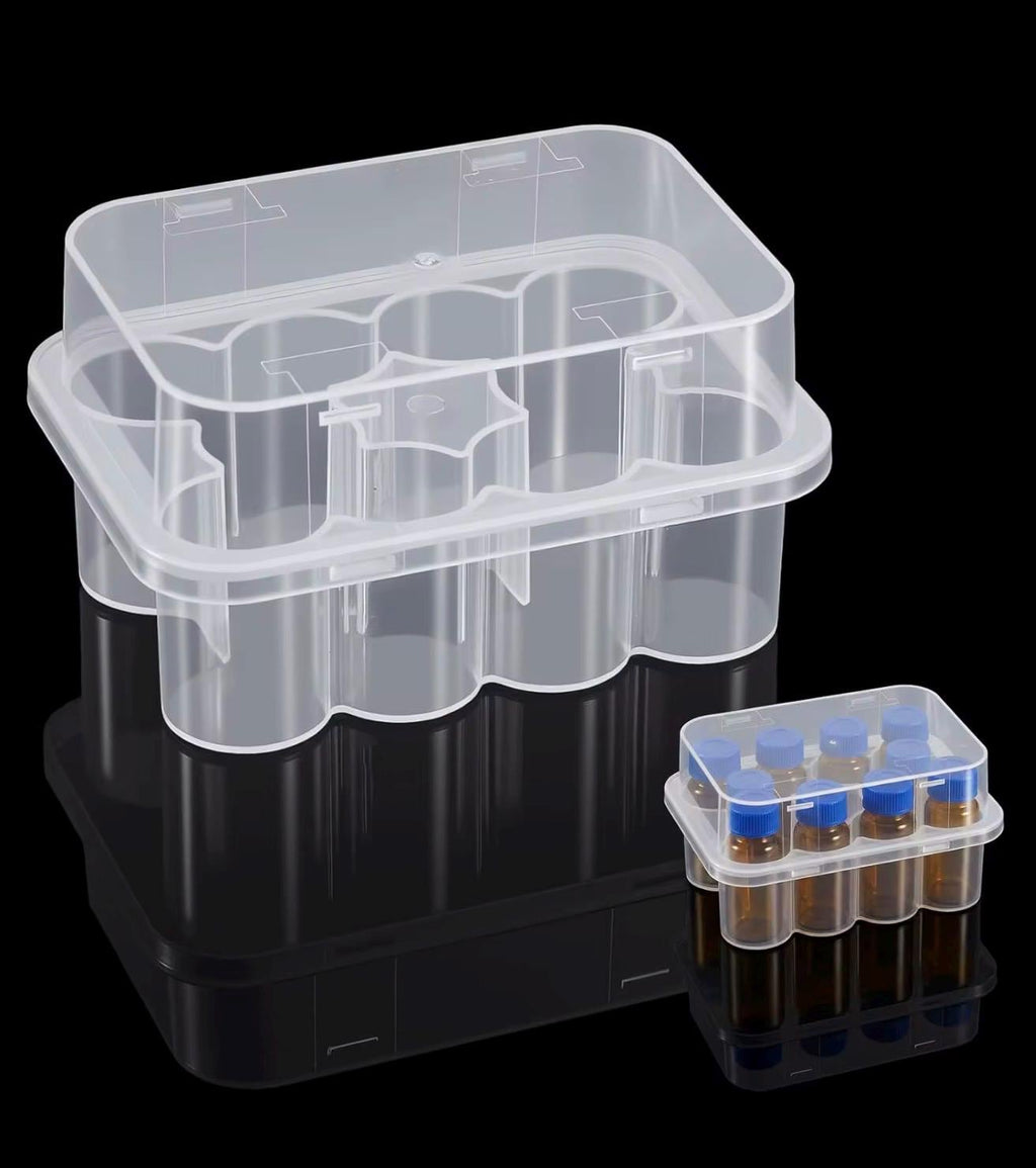 A large, empty, rectangular, clear plastic storage container with a hinged lid and internal dividers, positioned next to a smaller, filled, clear plastic storage container containing eight small amber glass vials with blue caps.